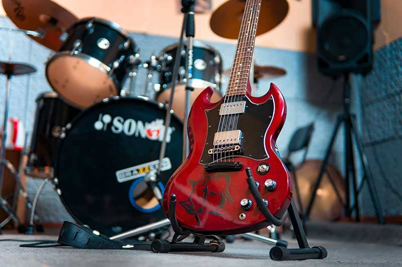 un guitare posée sur sono socle devant une batterie 